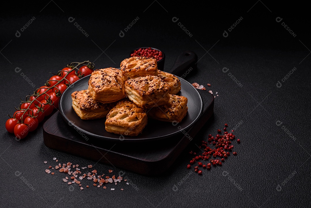 Folhados triangulares com queijo feta, tomate com sal, especiarias e ervas sobre fundo escuro de concreto