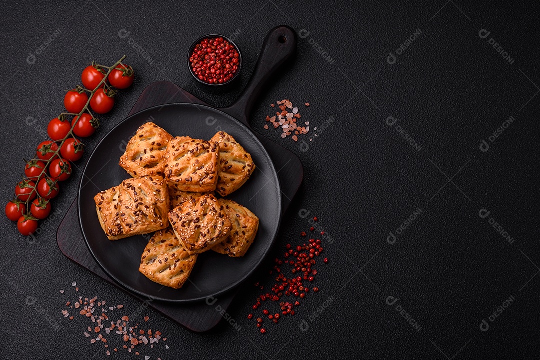 Folhados triangulares com queijo feta, tomate com sal, especiarias e ervas sobre fundo escuro de concreto