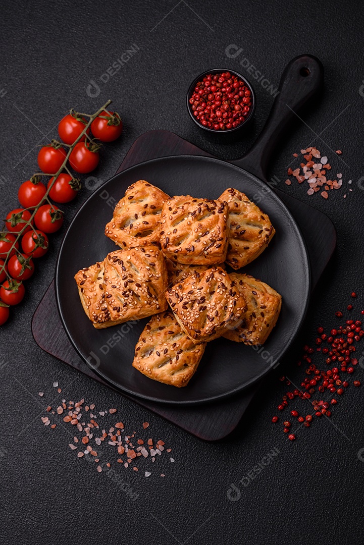 Folhados triangulares com queijo feta, tomate com sal, especiarias e ervas sobre fundo escuro de concreto