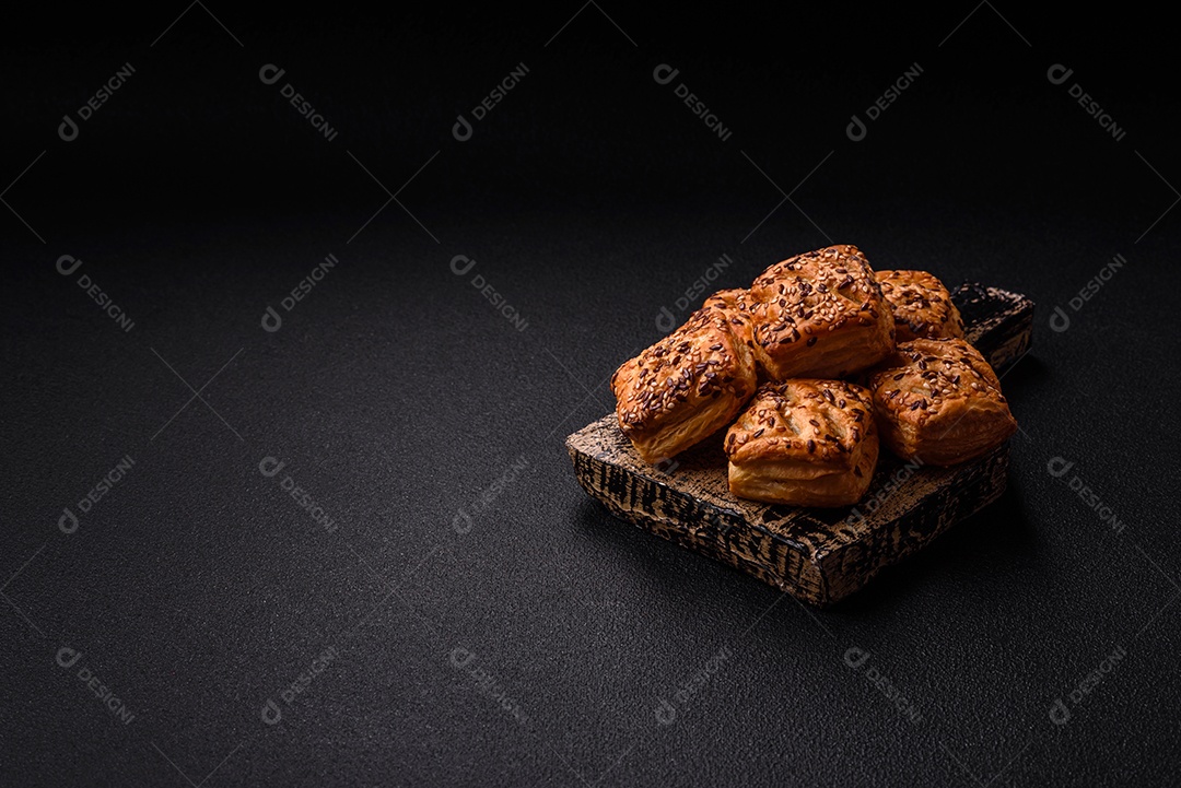 Folhados triangulares com queijo feta, tomate com sal, especiarias e ervas sobre fundo escuro de concreto
