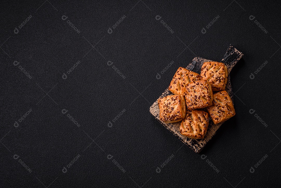 Folhados triangulares com queijo feta, tomate com sal, especiarias e ervas sobre fundo escuro de concreto