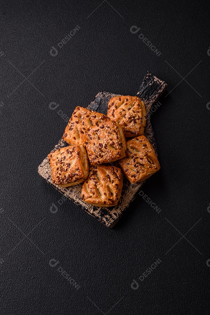 Folhados triangulares com queijo feta, tomate com sal, especiarias e ervas sobre fundo escuro de concreto