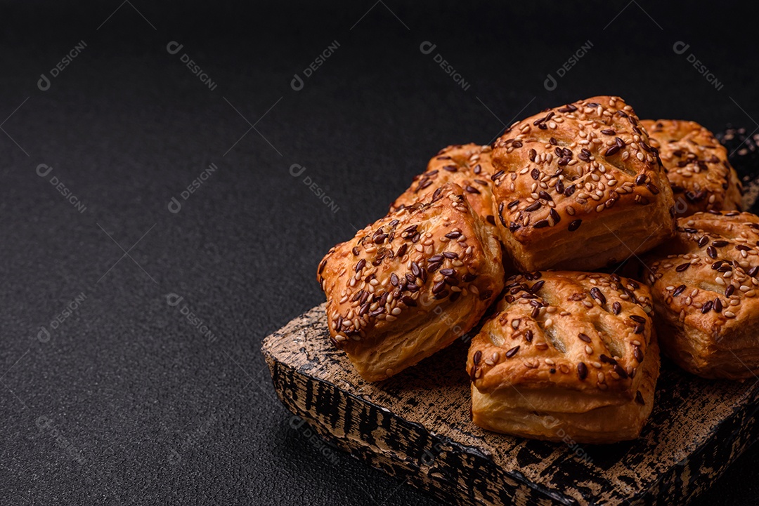 Folhados triangulares com queijo feta, tomate com sal, especiarias e ervas sobre fundo escuro de concreto