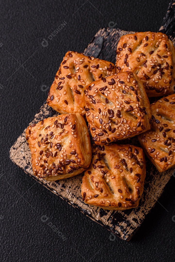 Folhados triangulares com queijo feta, tomate com sal, especiarias e ervas sobre fundo escuro de concreto