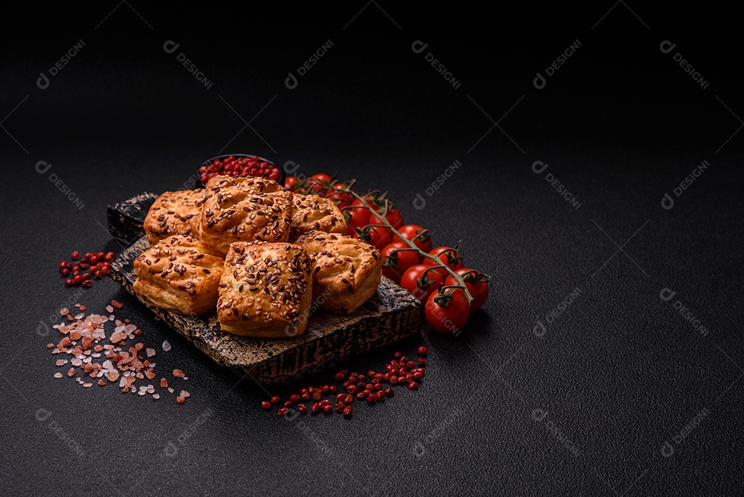 Folhados triangulares com queijo feta, tomate com sal, especiarias e ervas sobre fundo escuro de concreto