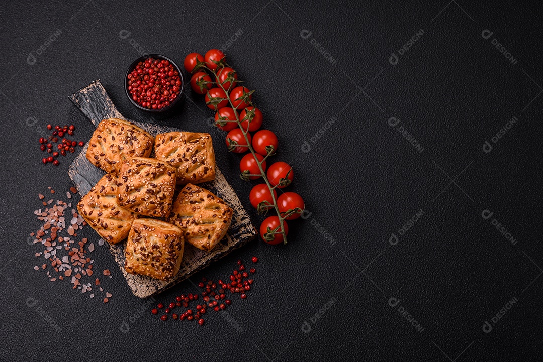 Folhados triangulares com queijo feta, tomate com sal, especiarias e ervas sobre fundo escuro de concreto