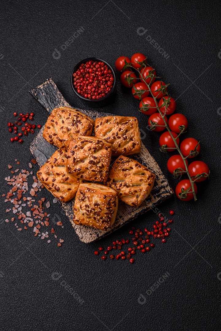 Folhados triangulares com queijo feta, tomate com sal, especiarias e ervas sobre fundo escuro de concreto