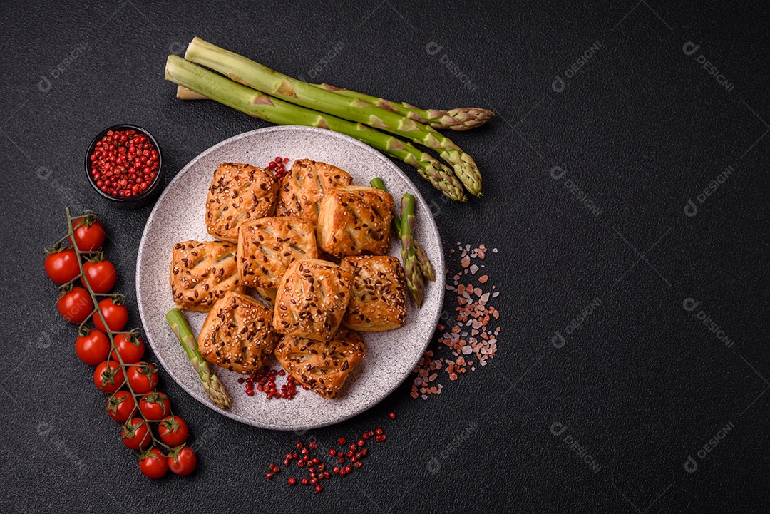 Folhados triangulares com queijo feta, tomate com sal, especiarias e ervas sobre fundo escuro de concreto