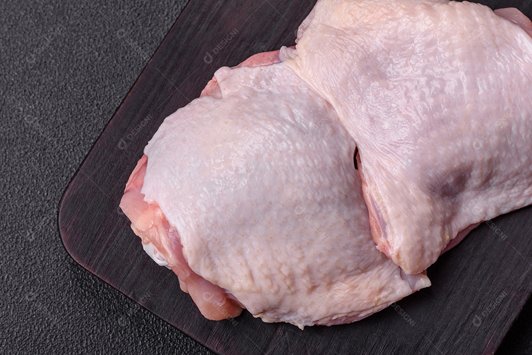 Pernas de frango cru com sal, especiarias e ervas sobre um fundo escuro de concreto