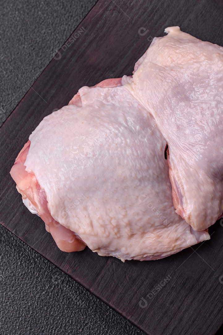 Pernas de frango cru com sal, especiarias e ervas sobre um fundo escuro de concreto