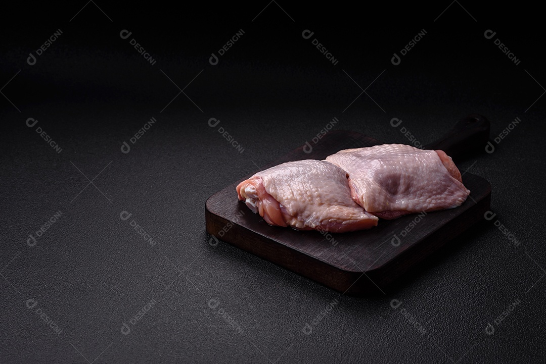 Pernas de frango cru com sal, especiarias e ervas sobre um fundo escuro de concreto