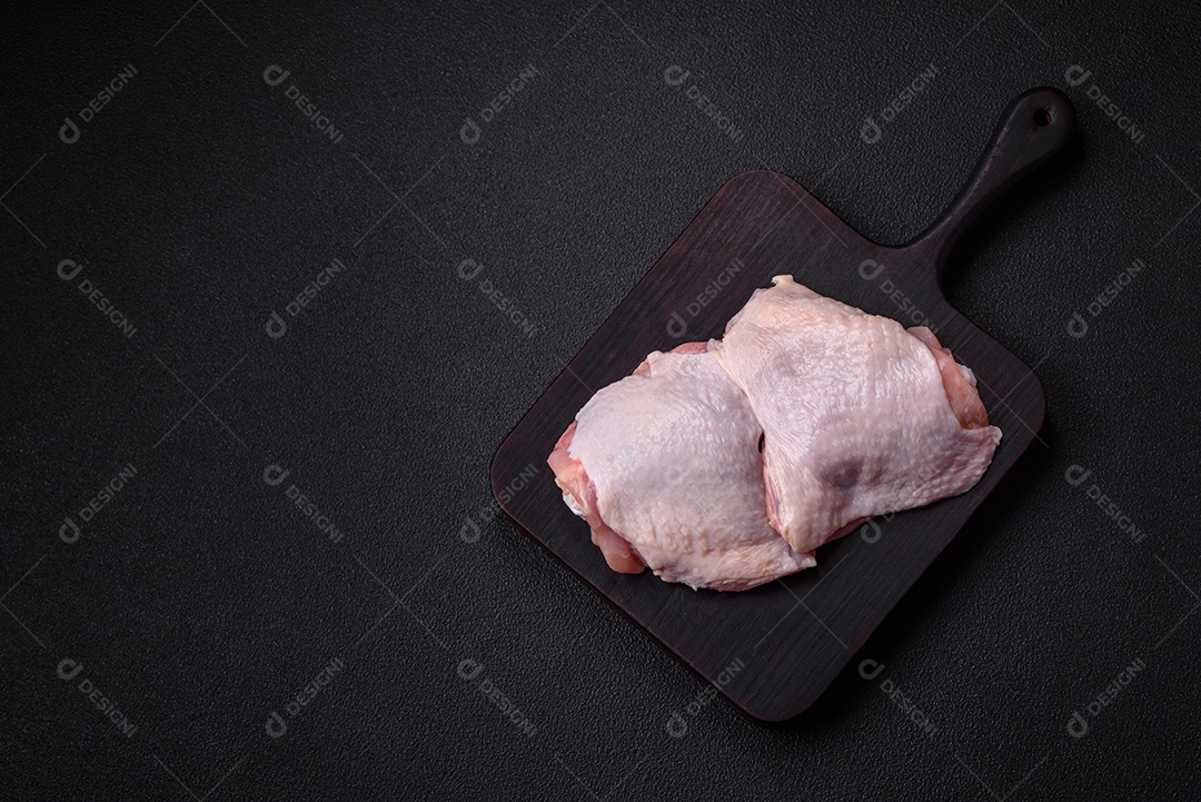 Pernas de frango cru com sal, especiarias e ervas sobre um fundo escuro de concreto