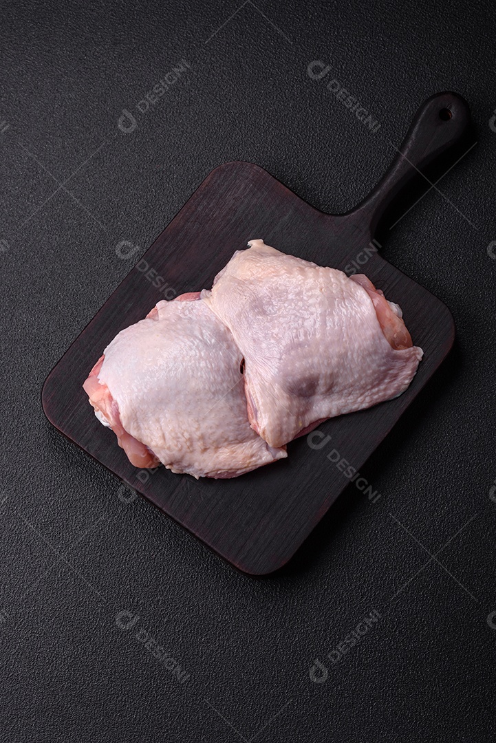 Pernas de frango cru com sal, especiarias e ervas sobre um fundo escuro de concreto