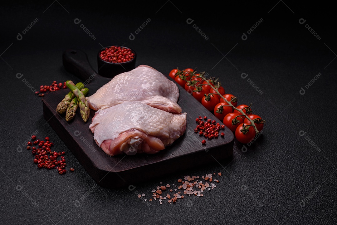 Pernas de frango cru com sal, especiarias e ervas sobre um fundo escuro de concreto