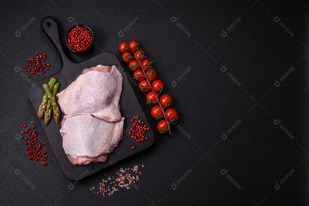 Pernas de frango cru com sal, especiarias e ervas sobre um fundo escuro de concreto