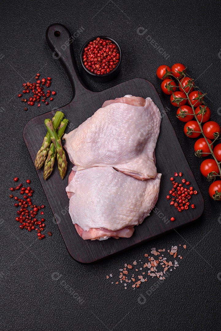 Pernas de frango cru com sal, especiarias e ervas sobre um fundo escuro de concreto