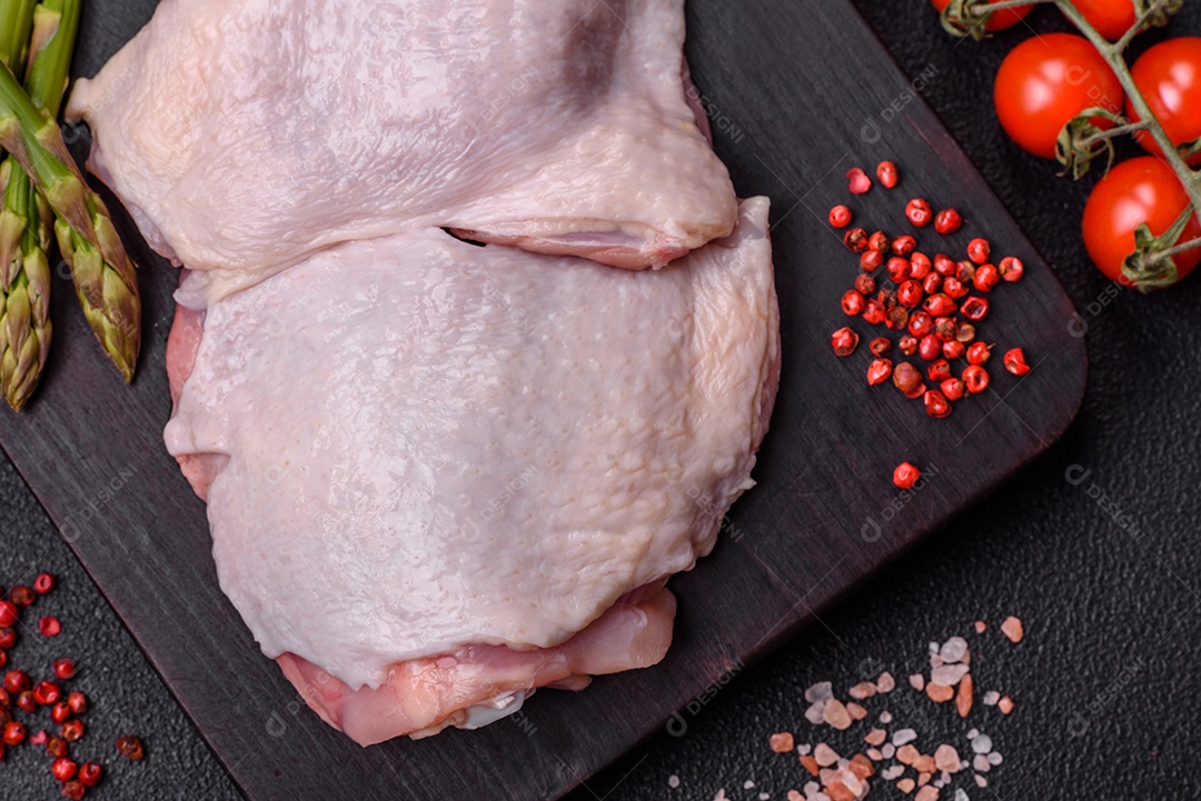 Pernas de frango cru com sal, especiarias e ervas sobre um fundo escuro de concreto