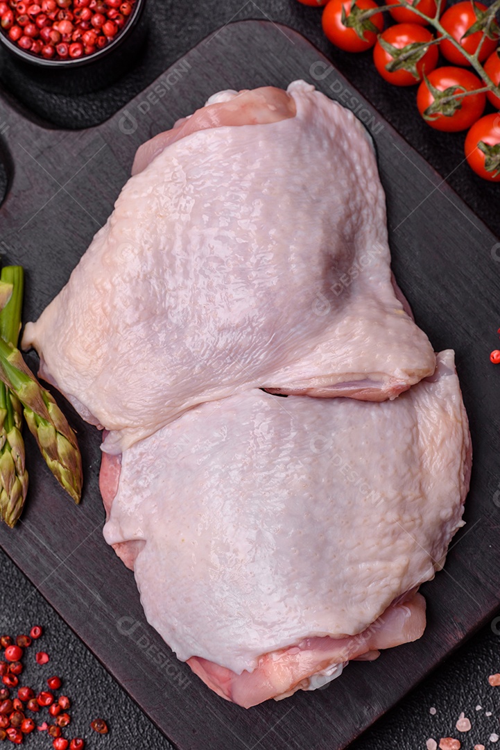 Pernas de frango cru com sal, especiarias e ervas sobre um fundo escuro de concreto