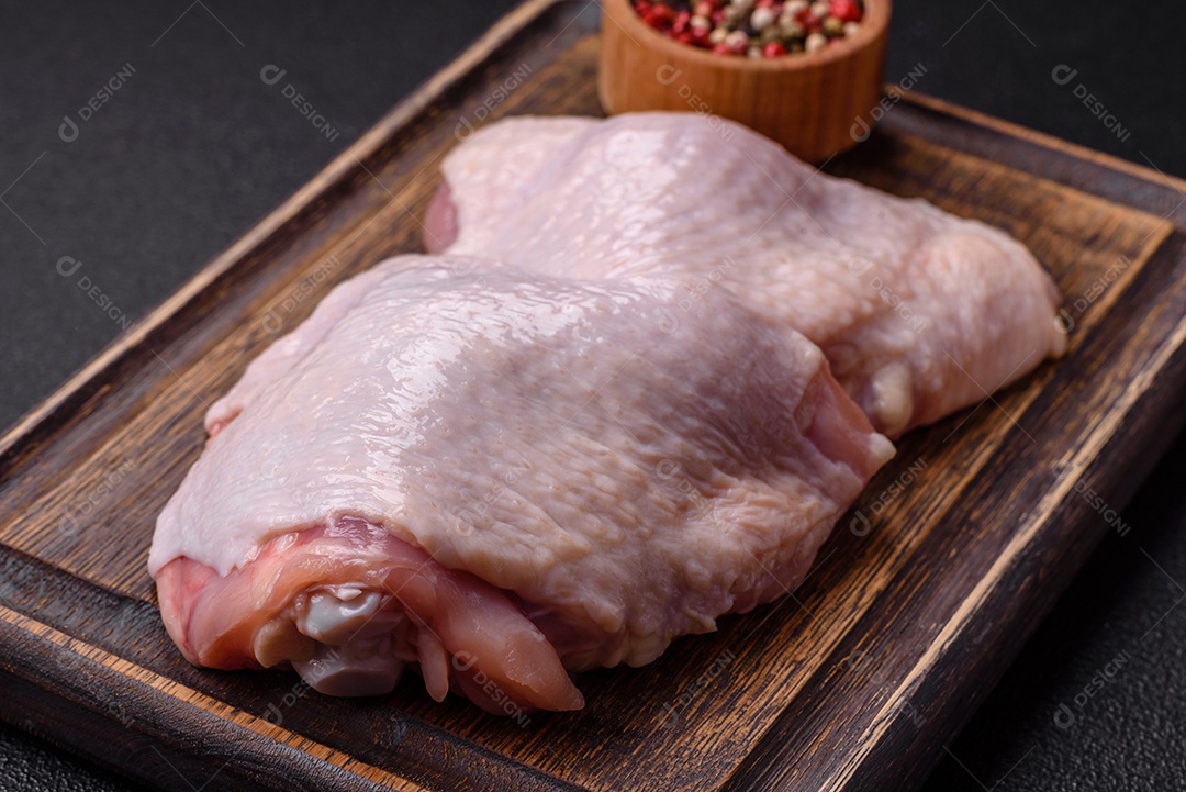 Pernas de frango cru com sal, especiarias e ervas sobre um fundo escuro de concreto