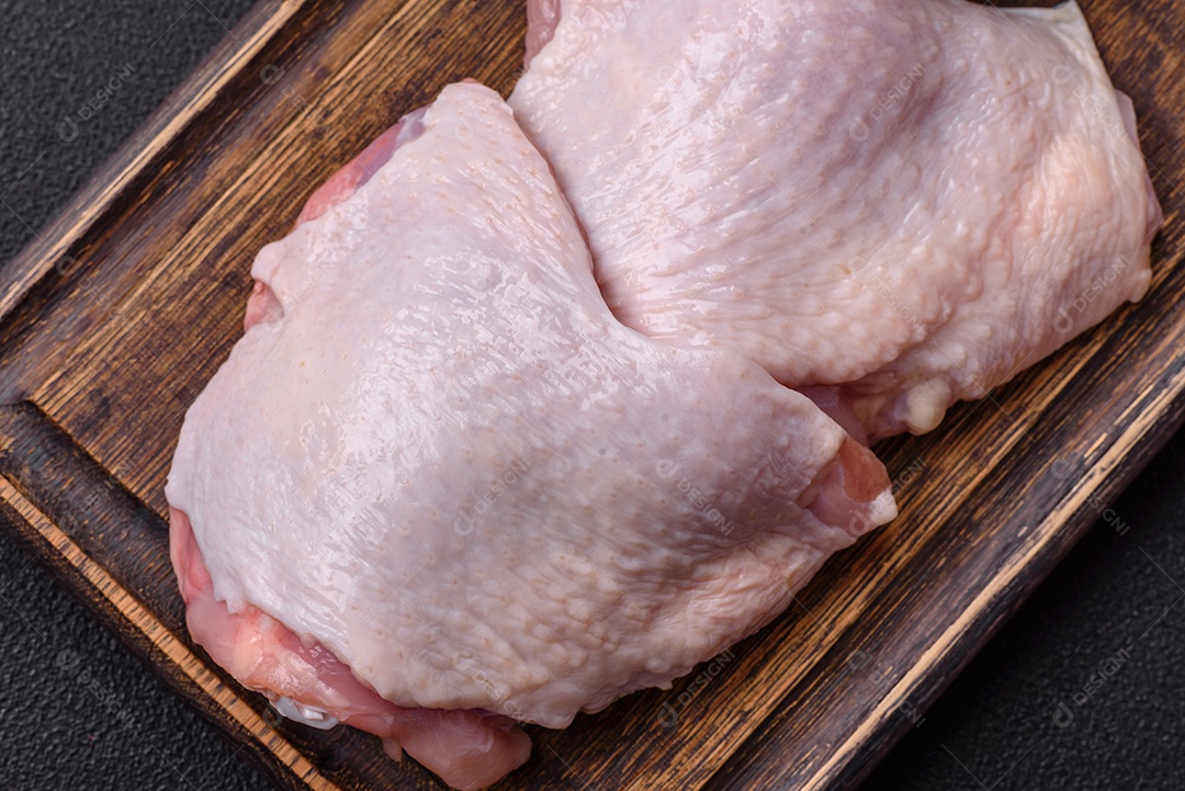 Pernas de frango cru com sal, especiarias e ervas sobre um fundo escuro de concreto