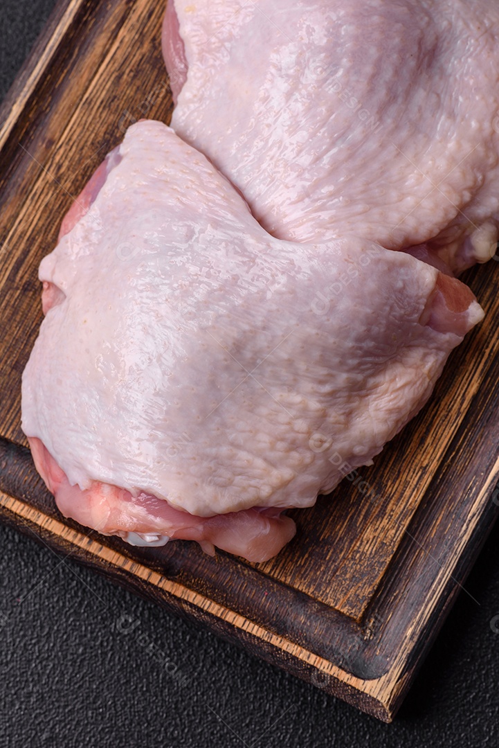 Pernas de frango cru com sal, especiarias e ervas sobre um fundo escuro de concreto