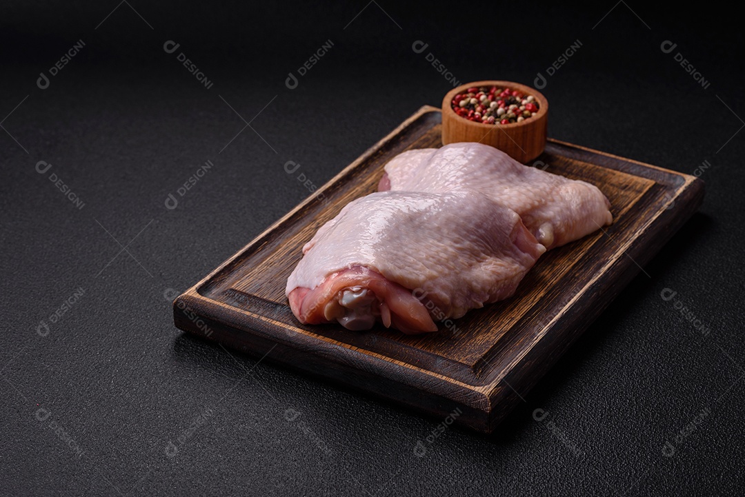 Pernas de frango cru com sal, especiarias e ervas sobre um fundo escuro de concreto