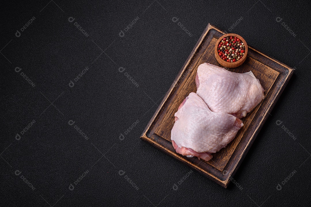 Pernas de frango cru com sal, especiarias e ervas sobre um fundo escuro de concreto