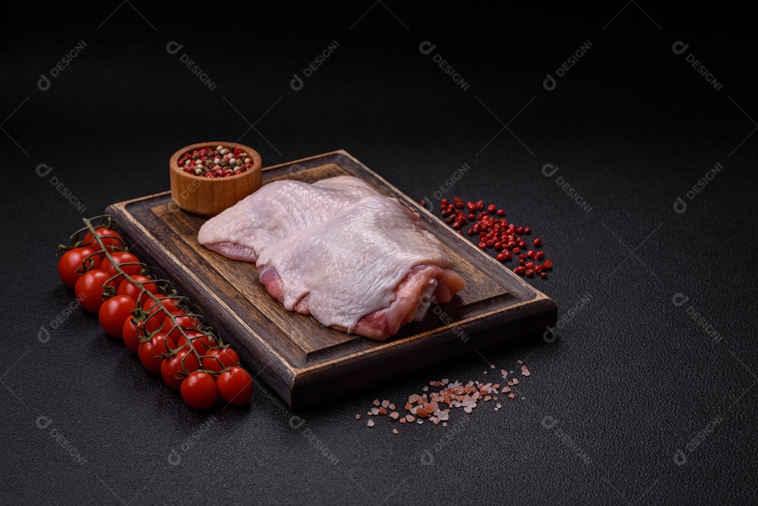 Pernas de frango cru com sal, especiarias e ervas sobre um fundo escuro de concreto