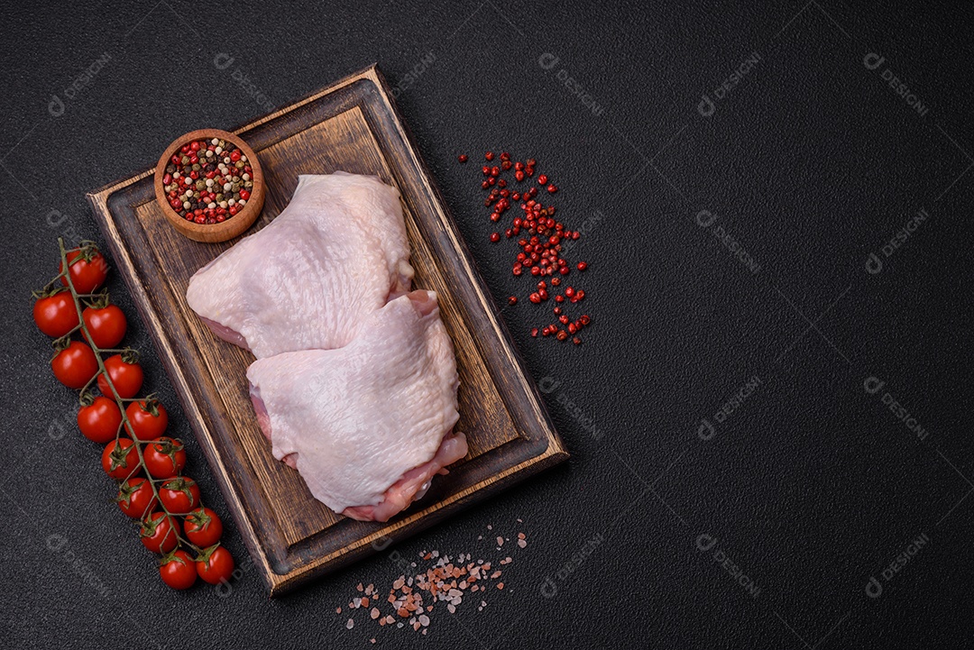 Pernas de frango cru com sal, especiarias e ervas sobre um fundo escuro de concreto