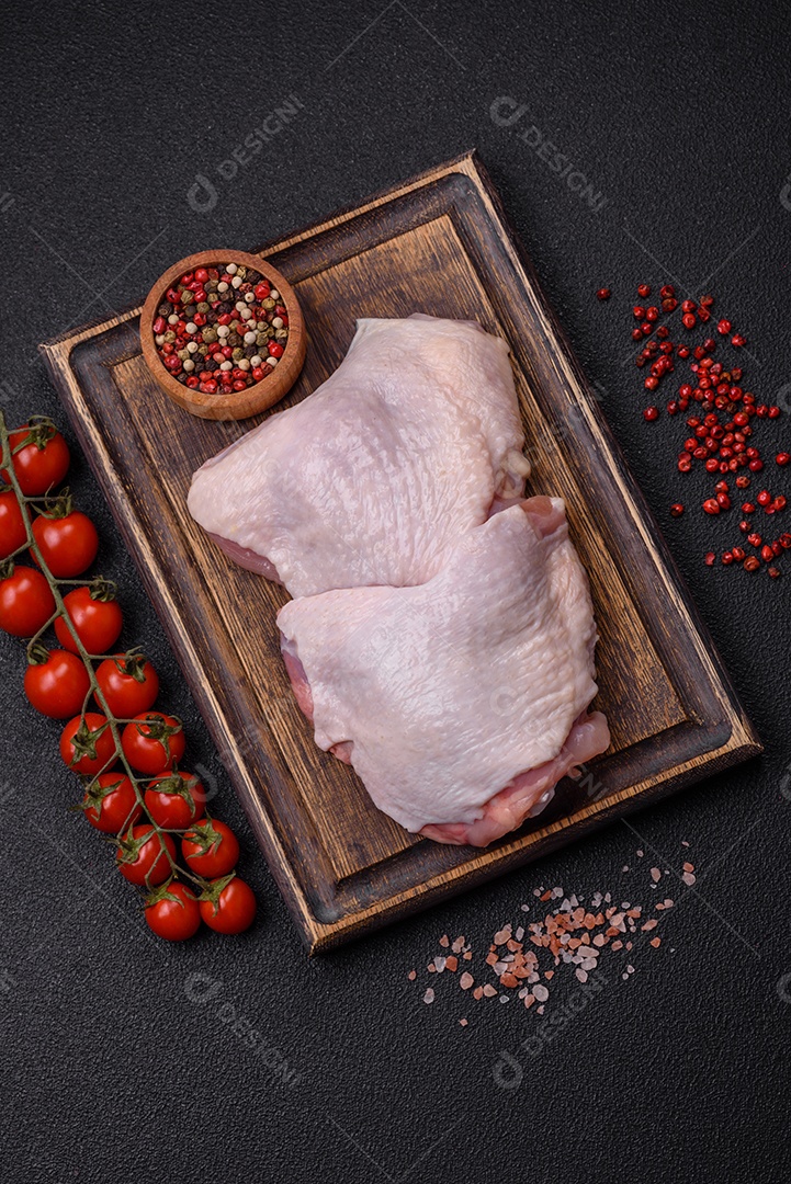 Pernas de frango cru com sal, especiarias e ervas sobre um fundo escuro de concreto