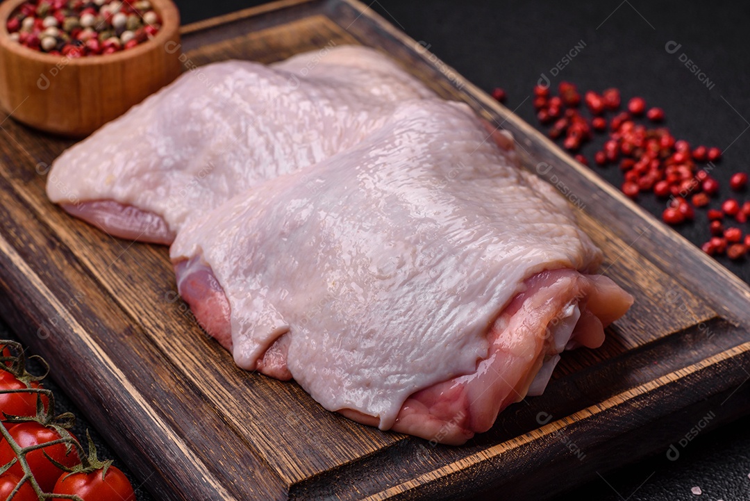 Pernas de frango cru com sal, especiarias e ervas sobre um fundo escuro de concreto