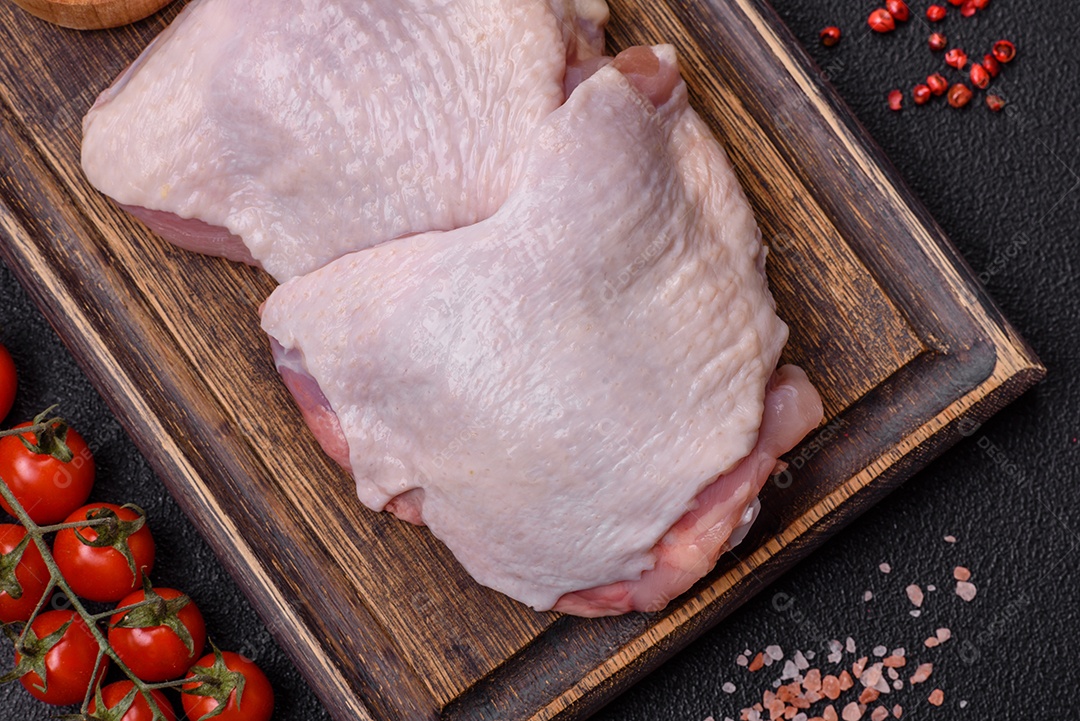 Pernas de frango cru com sal, especiarias e ervas sobre um fundo escuro de concreto