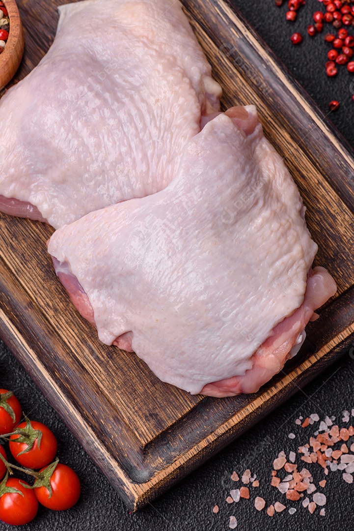 Pernas de frango cru com sal, especiarias e ervas sobre um fundo escuro de concreto