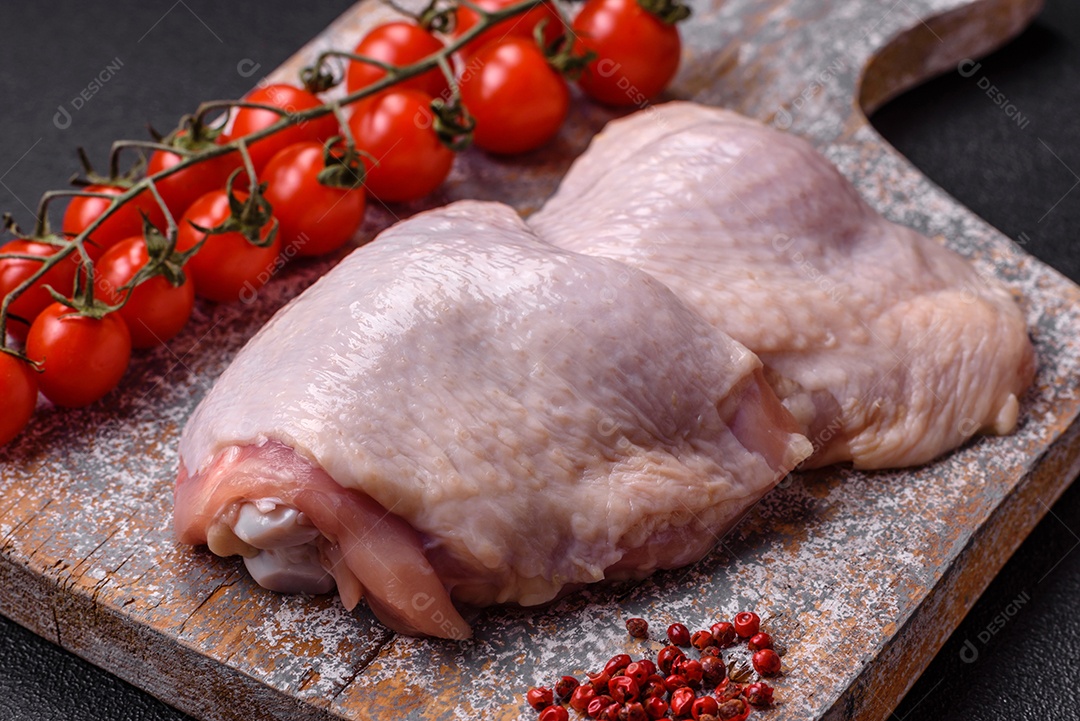 Pernas de frango cru com sal, especiarias e ervas sobre um fundo escuro de concreto