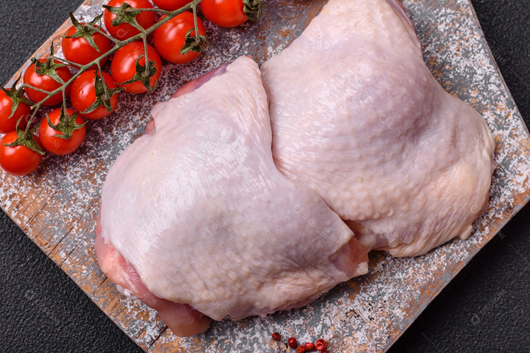 Pernas de frango cru com sal, especiarias e ervas sobre um fundo escuro de concreto
