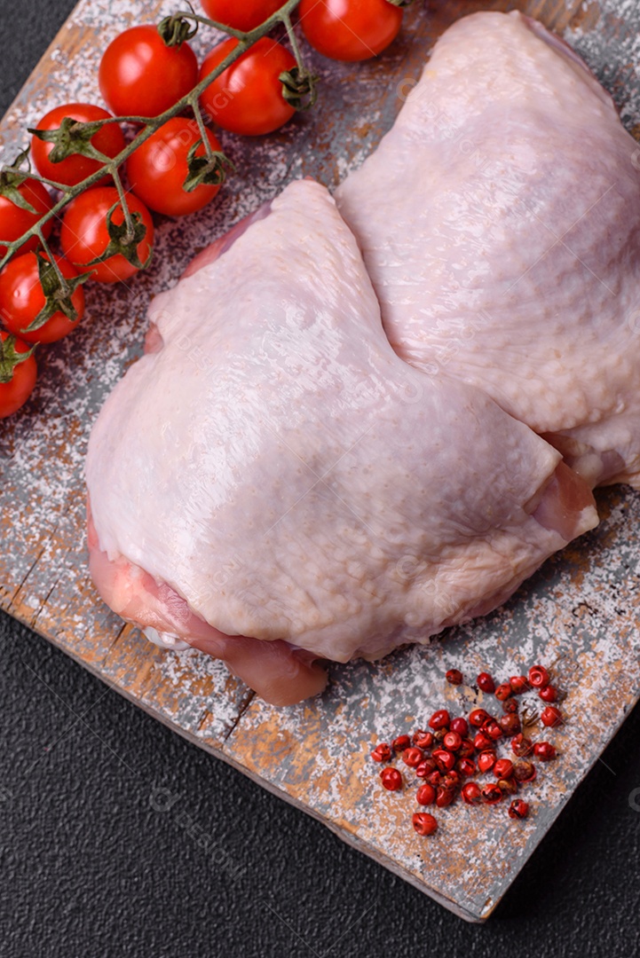 Pernas de frango cru com sal, especiarias e ervas sobre um fundo escuro de concreto