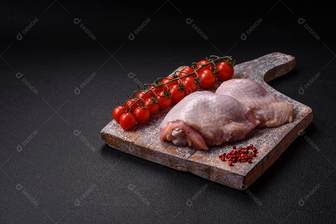 Pernas de frango cru com sal, especiarias e ervas sobre um fundo escuro de concreto