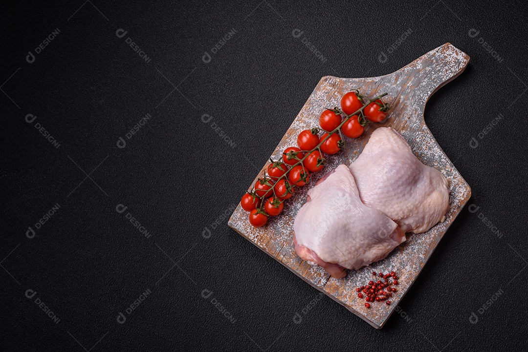 Pernas de frango cru com sal, especiarias e ervas sobre um fundo escuro de concreto