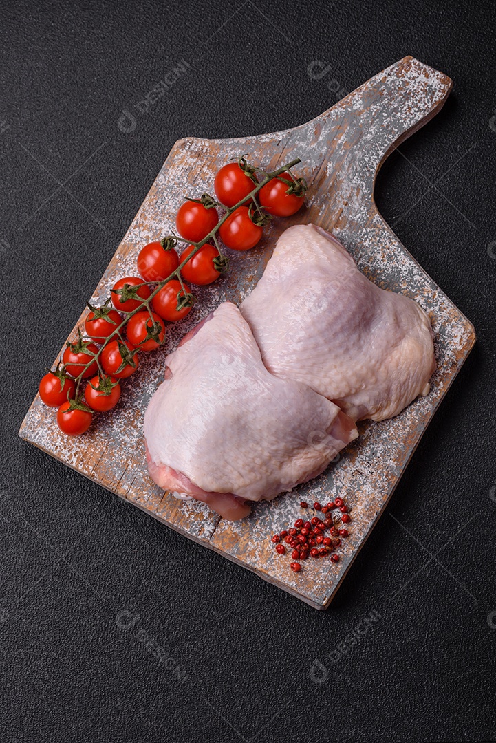 Pernas de frango cru com sal, especiarias e ervas sobre um fundo escuro de concreto