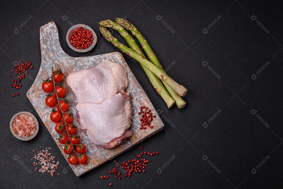 Pernas de frango cru com sal, especiarias e ervas sobre um fundo escuro de concreto