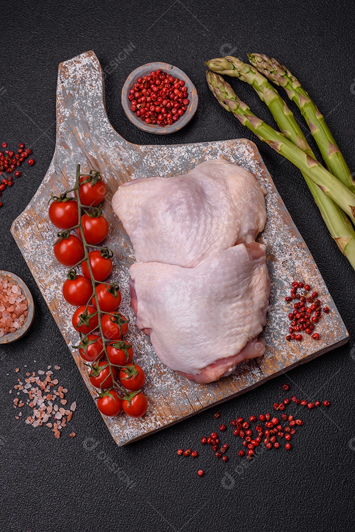 Pernas de frango cru com sal, especiarias e ervas sobre um fundo escuro de concreto