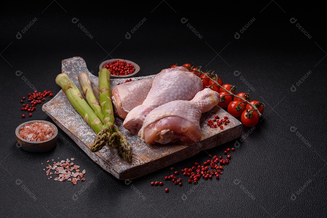 Pernas de frango cru com sal, especiarias e ervas sobre um fundo escuro de concreto