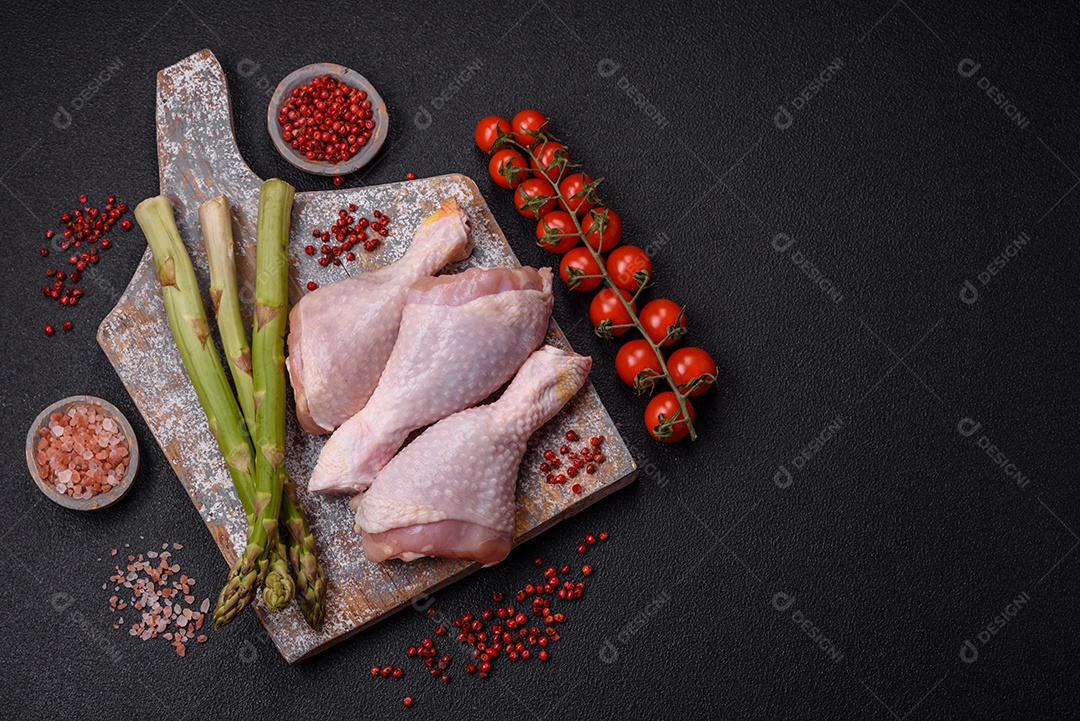 Pernas de frango cru com sal, especiarias e ervas sobre um fundo escuro de concreto