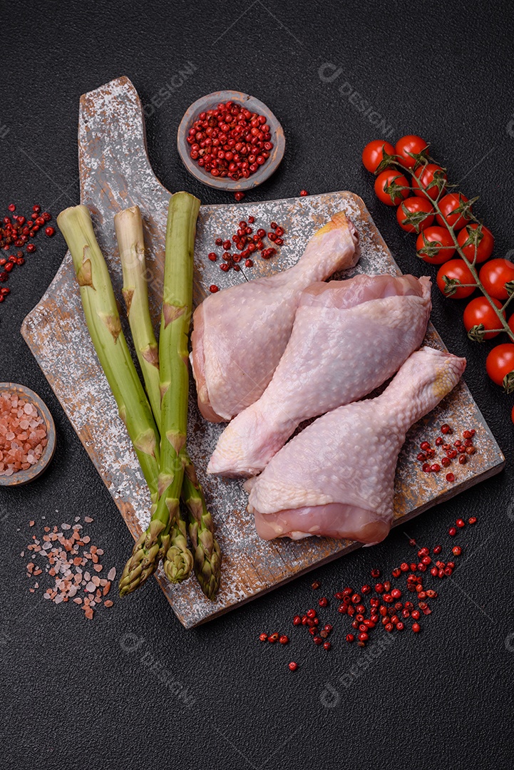 Pernas de frango cru com sal, especiarias e ervas sobre um fundo escuro de concreto