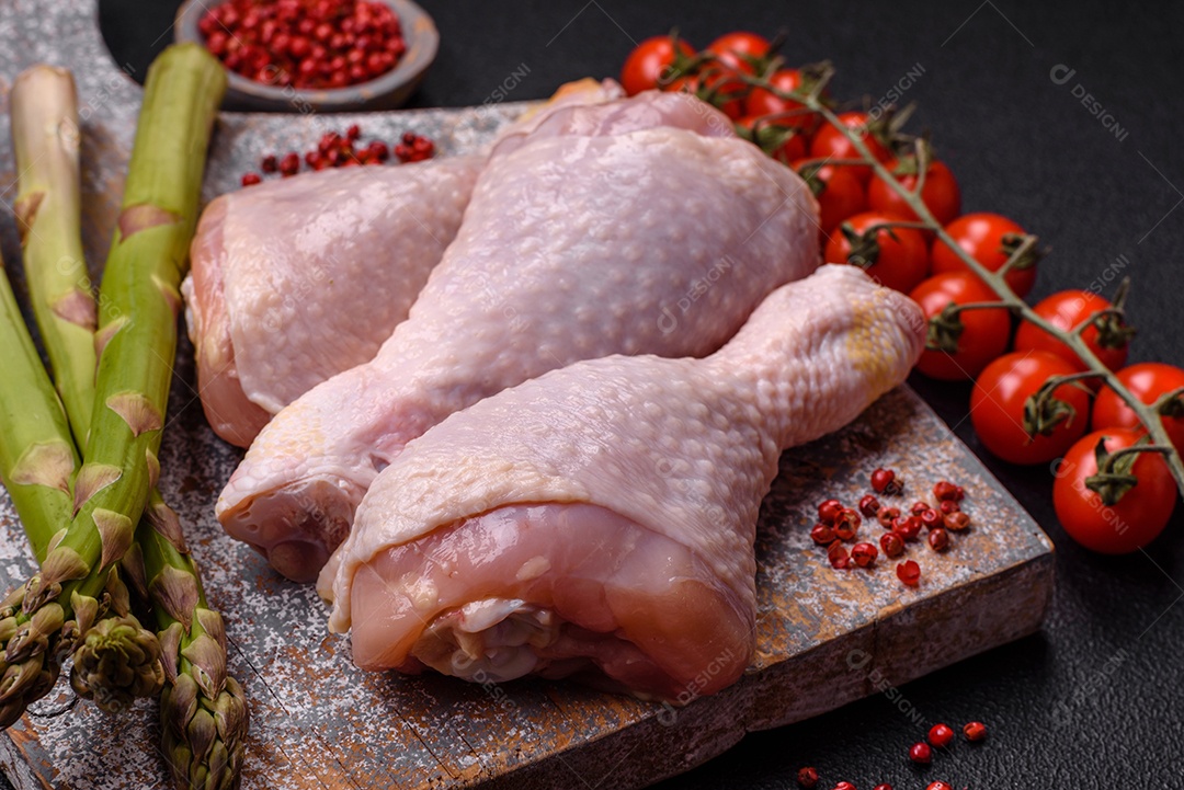 Pernas de frango cru com sal, especiarias e ervas sobre um fundo escuro de concreto