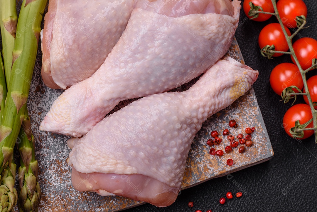 Pernas de frango cru com sal, especiarias e ervas sobre um fundo escuro de concreto