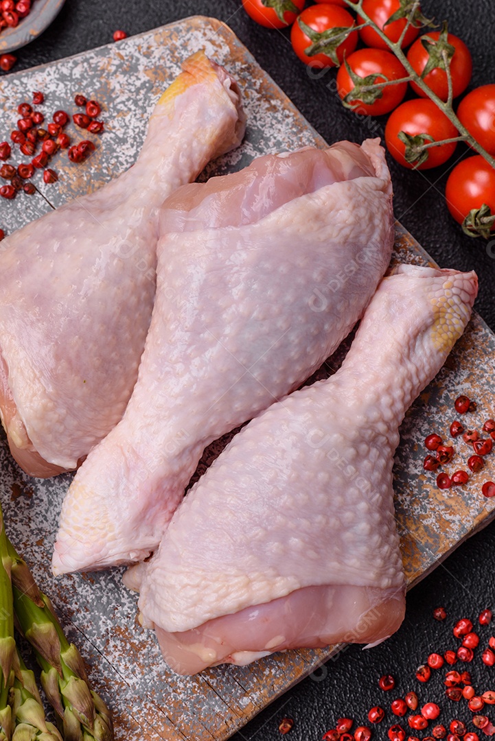 Pernas de frango cru com sal, especiarias e ervas sobre um fundo escuro de concreto