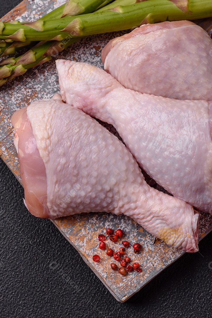 Pernas de frango cru com sal, especiarias e ervas sobre um fundo escuro de concreto