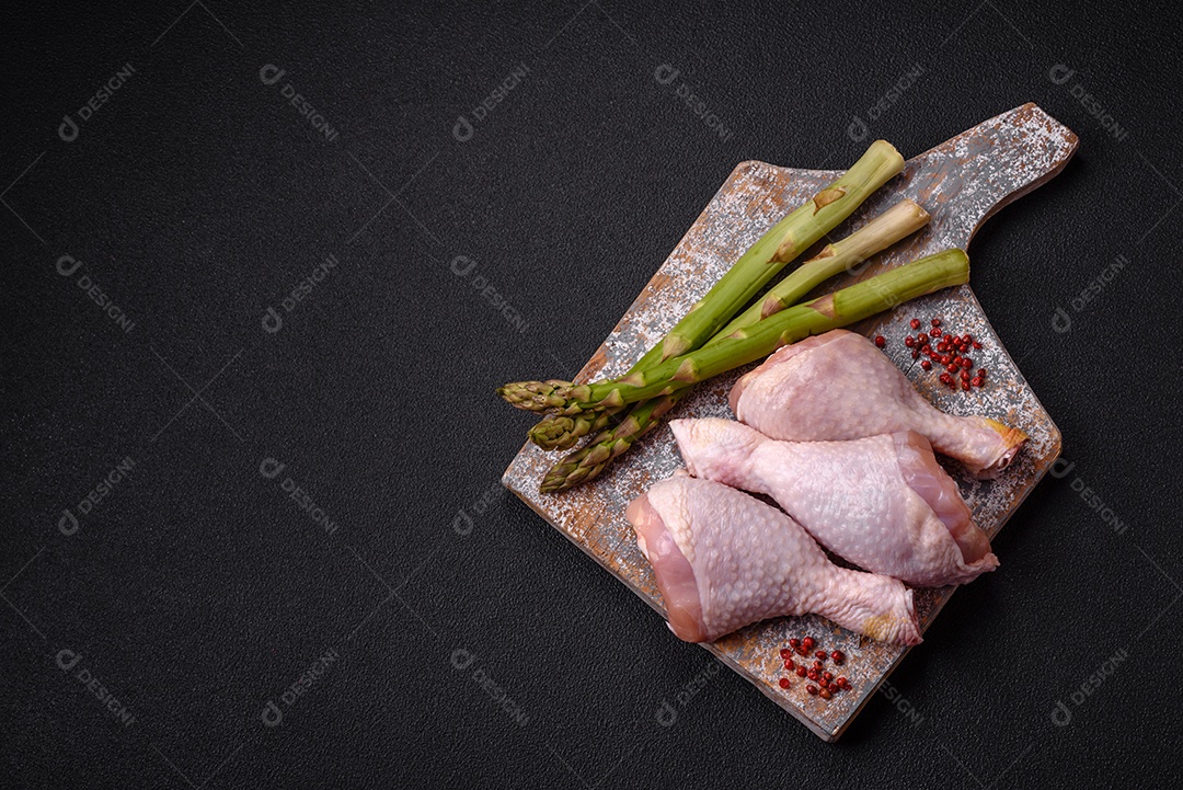 Pernas de frango cru com sal, especiarias e ervas sobre um fundo escuro de concreto