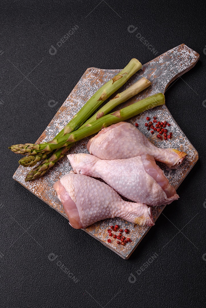 Pernas de frango cru com sal, especiarias e ervas sobre um fundo escuro de concreto